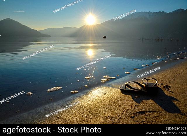 Flip Flops on the Sand Beach on Alpine Lake Maggiore with Sunlight and Mountain in Ascona, Switzerland