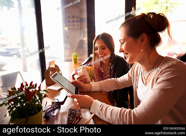 Toned picture of best friends ladies smiling whilespending their free time in cafe. Beautiful women using tablet PC and mobile or smart phone