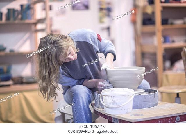 Female potter shaping clay bowl on pottery wheel