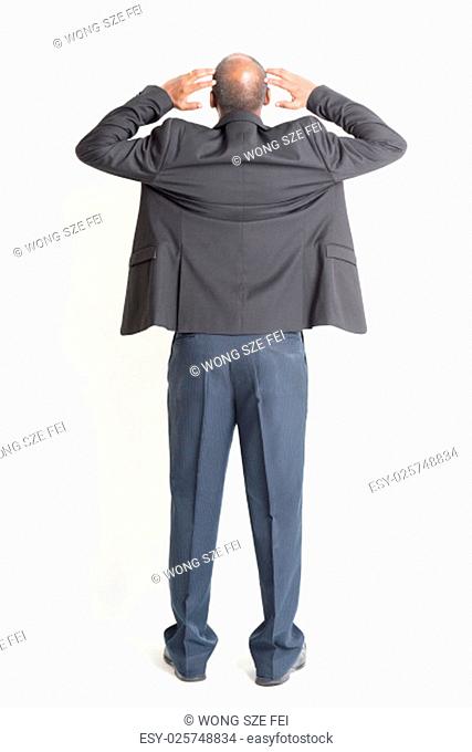 Rear view full body mature Indian business man hands scratching head , standing on plain background