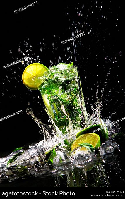 Fresh drink with splashesh of water, green mint and lime on black background