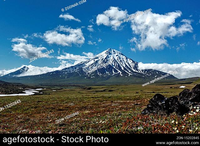Beautiful summer mountain landscape on sunny day with blue sky clouds: view of snowcapped cone of Mount Bolshaya Udina Volcano