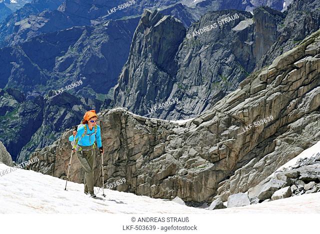 Woman ascending over snow, rocky mountains in background, Sentiero Roma, Bergell range, Lombardy, Italy