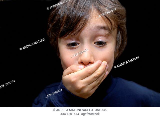 Male child keeping a secret with a hand over his mouth