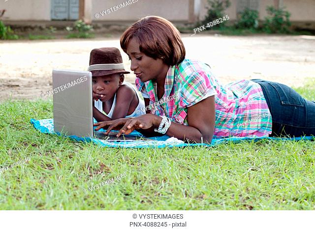 This woman and her son lying on the grass, working with her laptop