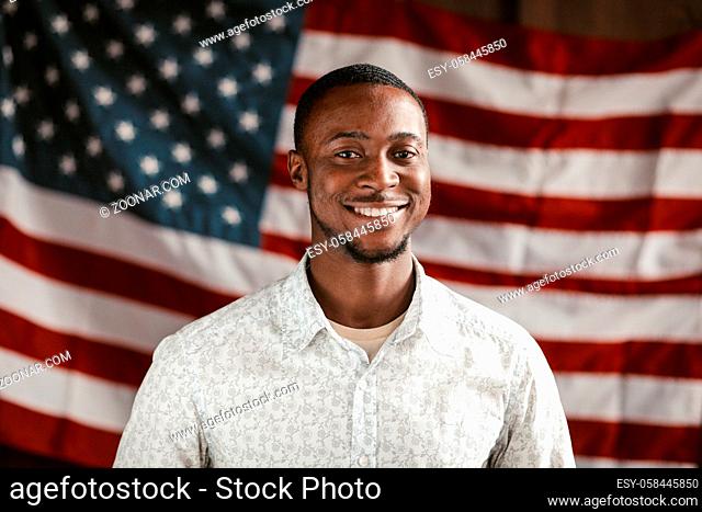 Charming Black Guy Dressed In White Shirt Cheerful Smiles Patriotically Posing On American Flag Background