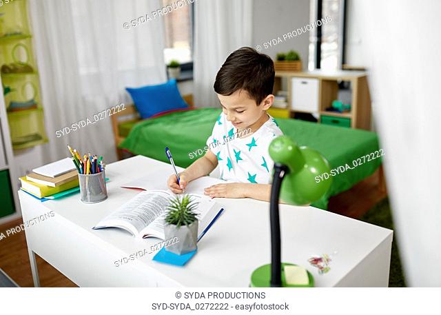 student boy with book writing to notebook at home