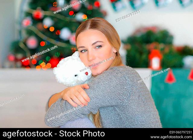 Portrait of a Nice Girl Spending Time at Home near Christmas Tree. Holding in Hands Little Present. Little Soft Toy. Teddy Bear. Happy Winter Holidays