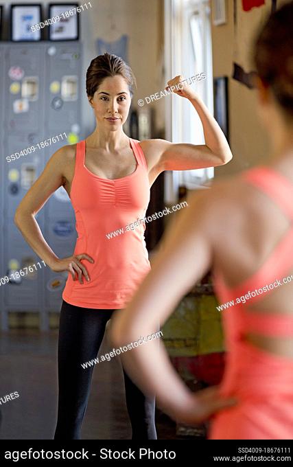 Strong confident woman looking in mirror while in gym flexing her arm