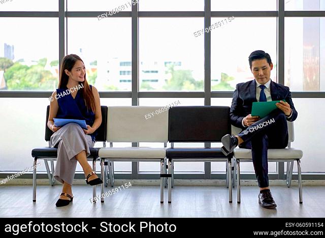 Young woman looks and smiles at a man sitting further away. Asian business people waiting for job interview by sitting spaced apart