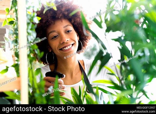 Smiling female florist spraying water on plant at shop