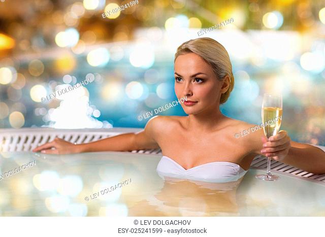 people, beauty, spa and relaxation concept - beautiful young woman wearing bikini swimsuit sitting with glass of champagne in jacuzzi at poolside over holidays...