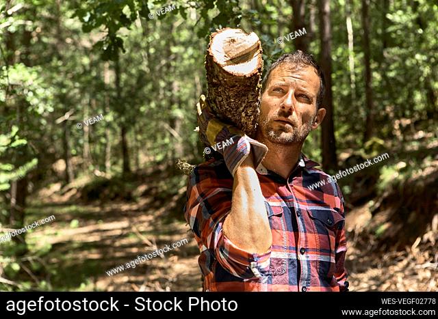 Thoughtful woodsman carrying log on shoulder while looking away in forest