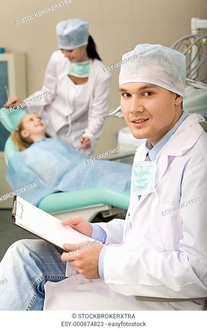 Image of sitting dentist with papers in hand looking at camera
