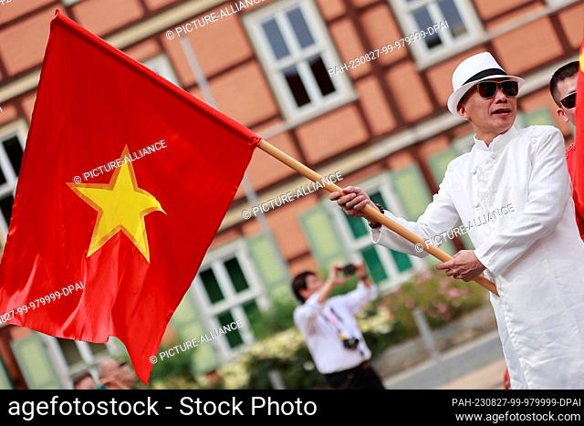 27 August 2023, Saxony-Anhalt, Wernigerode: Participants of a parade stand with a national flag of the socialist republic of Vietnam in front of the parade...