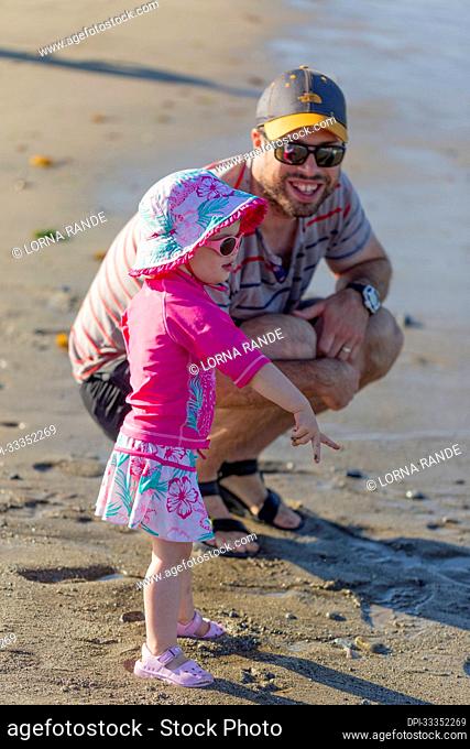 A father spends quality time with his toddler daughter at the water's edge at Ambleside Beach; West Vancouver, British Columbia, Canada