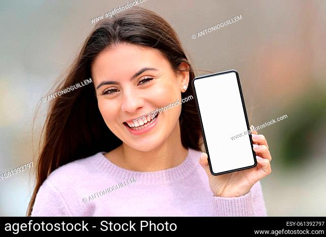 Front view portrait of a happy teen showing blank phone screen outdoors in the street