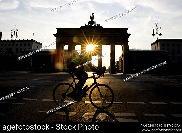 19 August 2023, Berlin: A cyclist rides past the Brandenburg Gate as the sun rises. People in Berlin and Brandenburg have to prepare for strong to extreme heat...