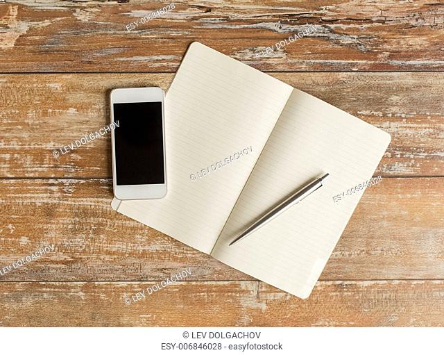 business, education, objects and technology concept - close up of notebook, pen and smartphone on table