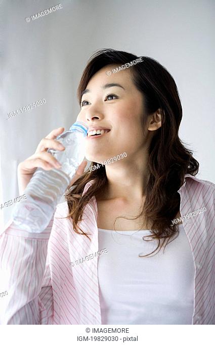 Young woman holding a bottle of water to her lips, smiling, close-up