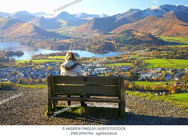 Female walkers sitting on a bench looking at the view above Derwentwater in the Lake District National Park with the Northern Fells in background