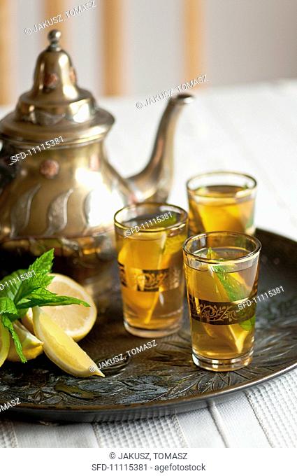 Three glasses of tea with mint and lemon and a teapot