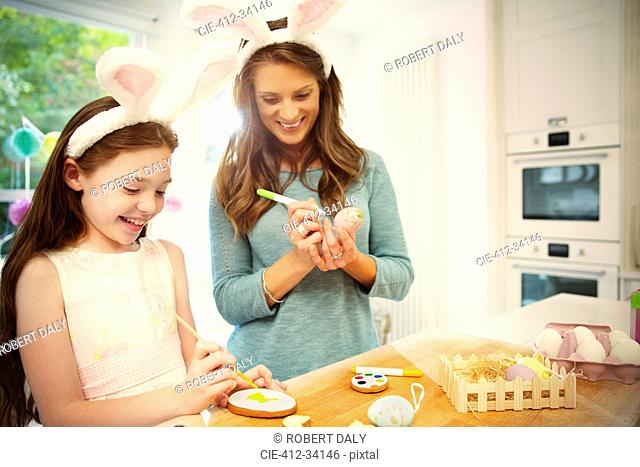 Mother and daughter wearing costume rabbit ears coloring Easter eggs and cookies