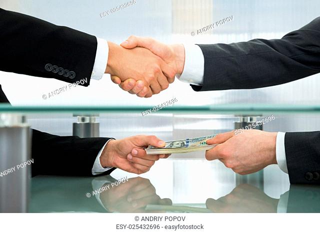 Close-up Of Businessman With Money Handshaking With His Business Partner
