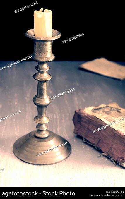 On the table, an old copper candlestick with a candle and an old book