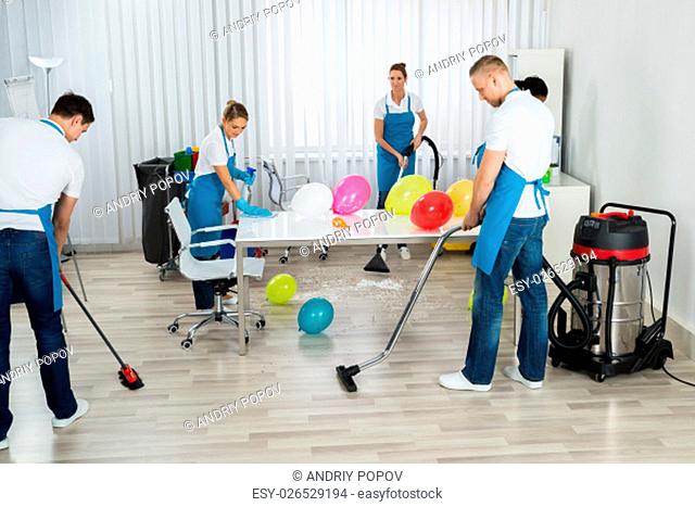 Group Of Male And Female Janitors Cleaning The Office After Party