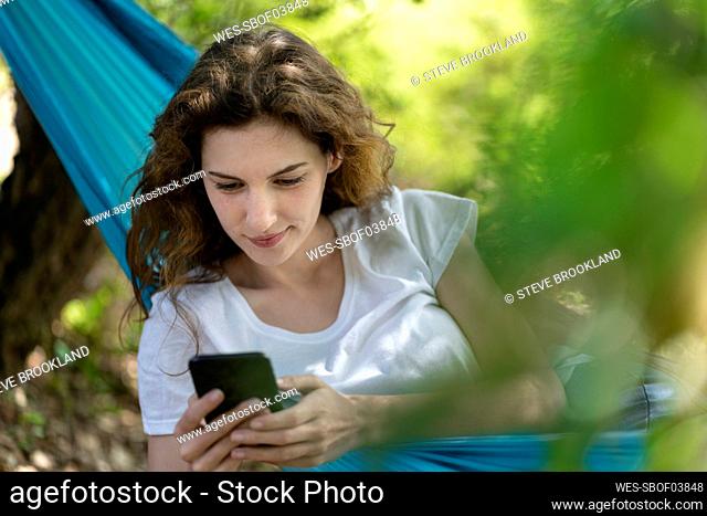 Young woman using smart phone while relaxing on hammock