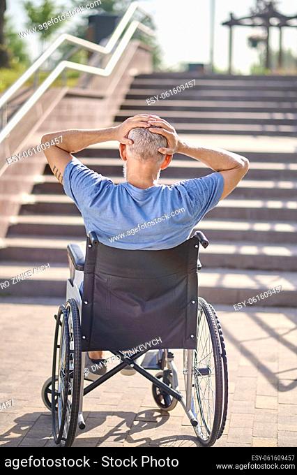 Disabled man. A man in a wheel chair sitting backside near the stairs outdoors