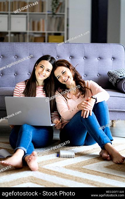 Smiling daughter with laptop sitting by mother on floor at home