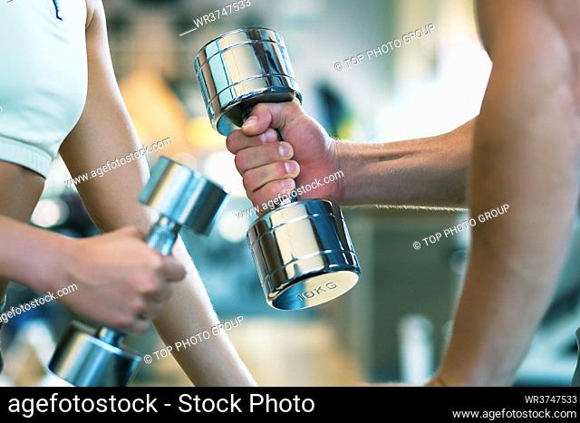 Two people (male / female) lifting dumbbells, shallow depth of field