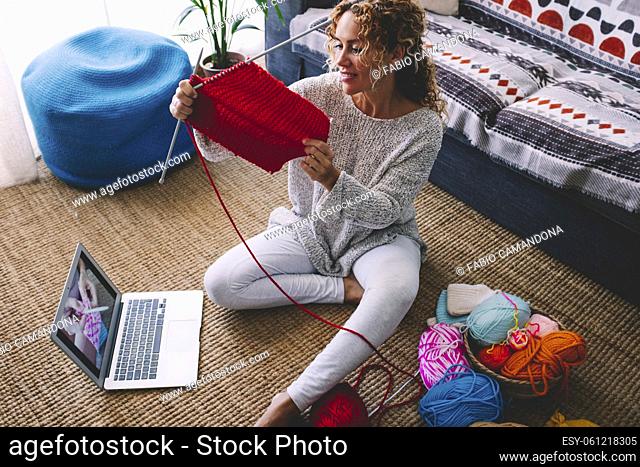 Modern woman do knit work at home thanks to video tutorial online content on laptop computer and wireless connection. Concept of new job opportunity and content...