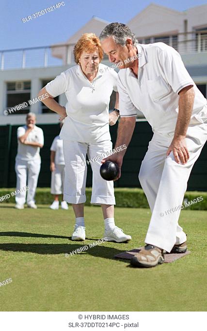Man teaching woman lawn bowling