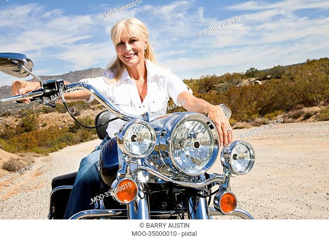 Senior woman sits on motorcycle on desert road