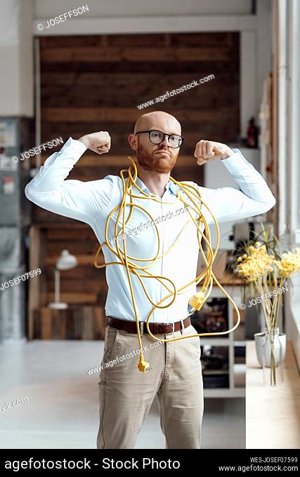 Confident young businessman covered with cable flexing muscles in office