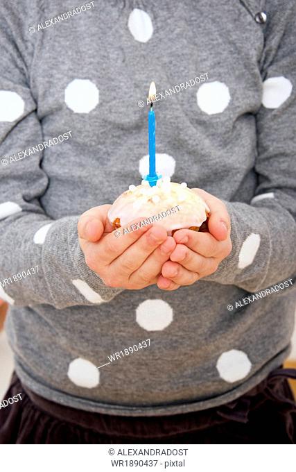 Child on birthday party holding cupcake with burning candle, Munich, Bavaria, Germany