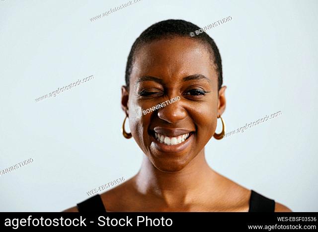 Young woman with short hair winking against white background