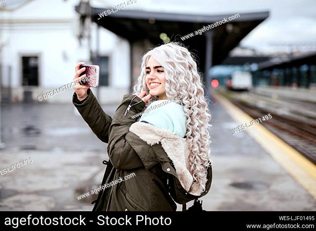 Portrait of smiling young woman taking selfie with smartphone on platform