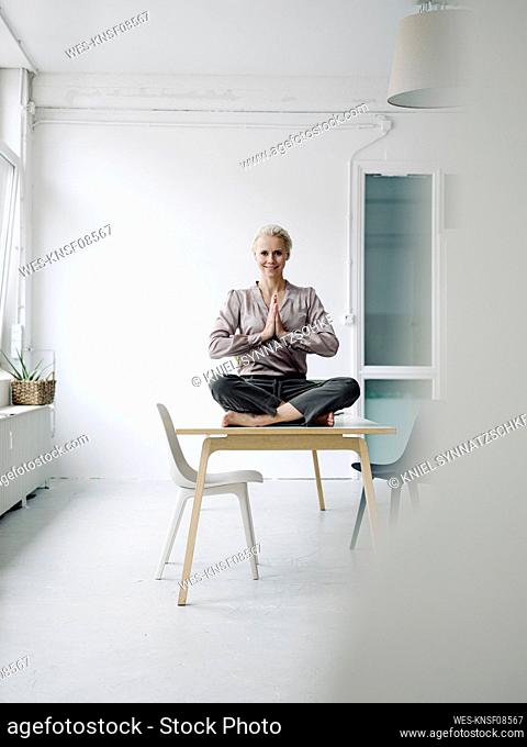 Businesswoman meditating while sitting on desk in office