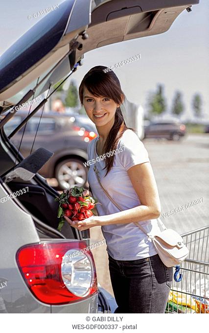 Portrait of smiling young woman loading purchase in her car