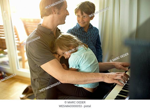 Father playing piano with daughter on his lap, son watching