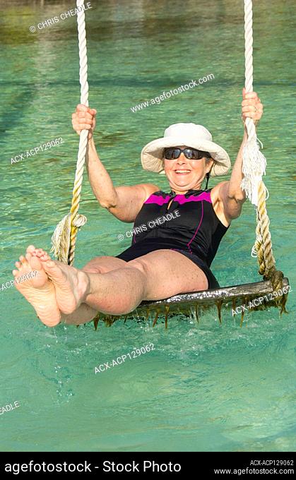 Woman enjoys swing in tropical waters and Palapa platforms, North Long Coco Plum Caye, Belize