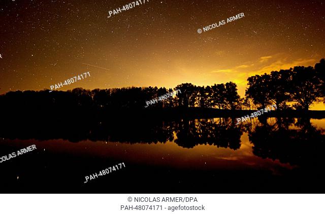 Trees surround a pond and a silhouetted against the evening sky near Hagenheim, Germany, 22 April 2014. The stars shine down from behind the clouds
