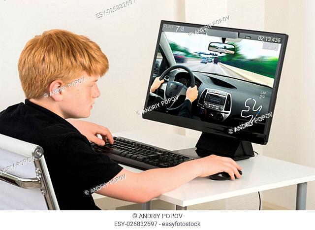 Boy Sitting On Chair Playing Car Game On Computer At Home