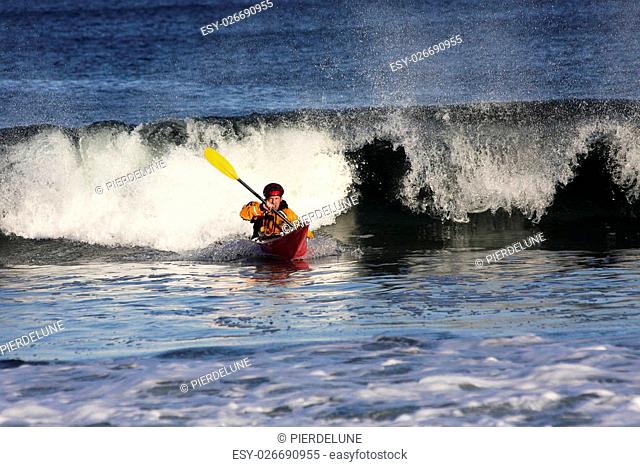 Kayak surfer with expressive face escaping from big wave on rough sea in Black Cove, Nova Scotia coast, Canada