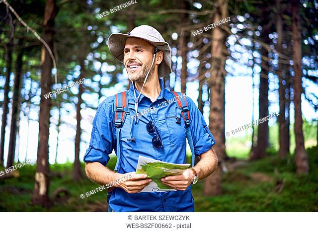Smiling man holding a map hiking in the forest
