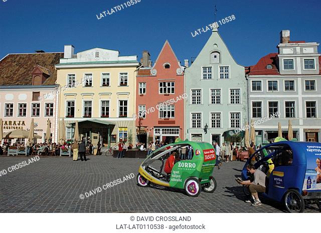 Cycle rickshaws. Brightly coloured bodywork. Town Hall Square, Raekoja Plats. Houses, cafes. People